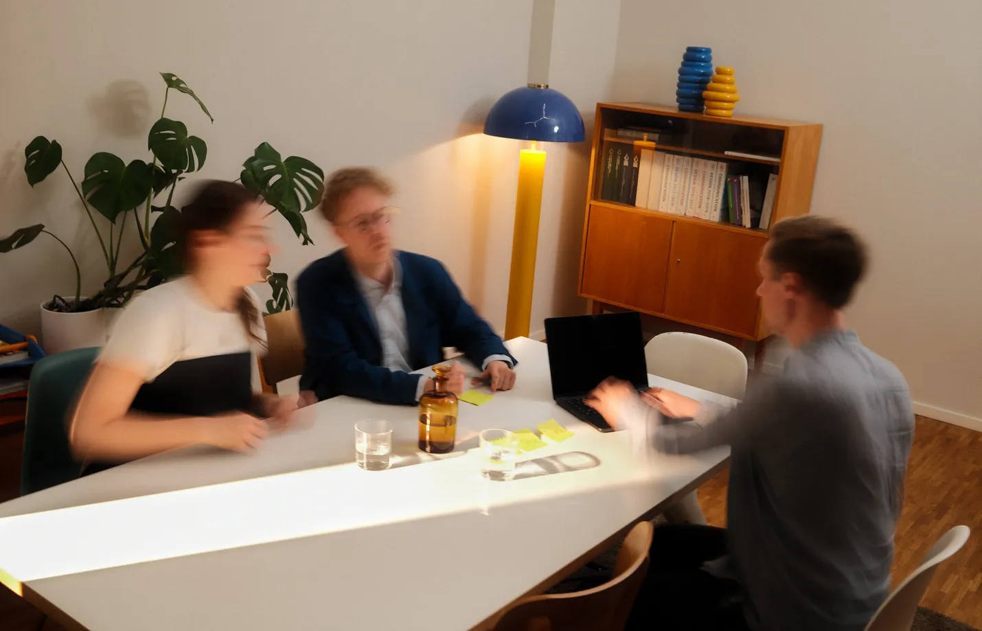 Three people at a team meeting at a white table with laptop and notes in a modern office