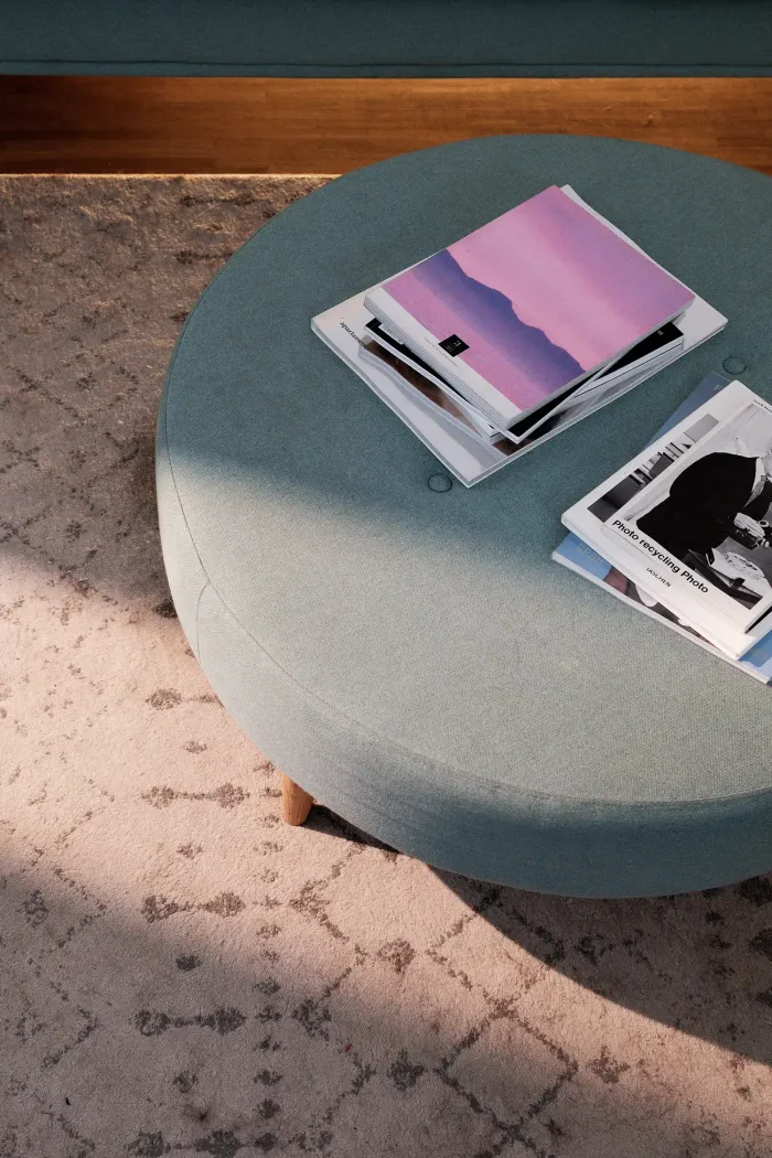 Round turquoise-coloured table with books and magazines on carpeted floor